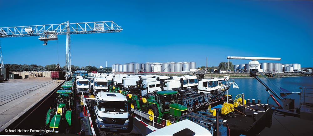Sicht auf die RoRo-Anlage im Rheinauhafen mit Traktoren und LKWs im Vordergrund bei strahlend blauem Himmel.
